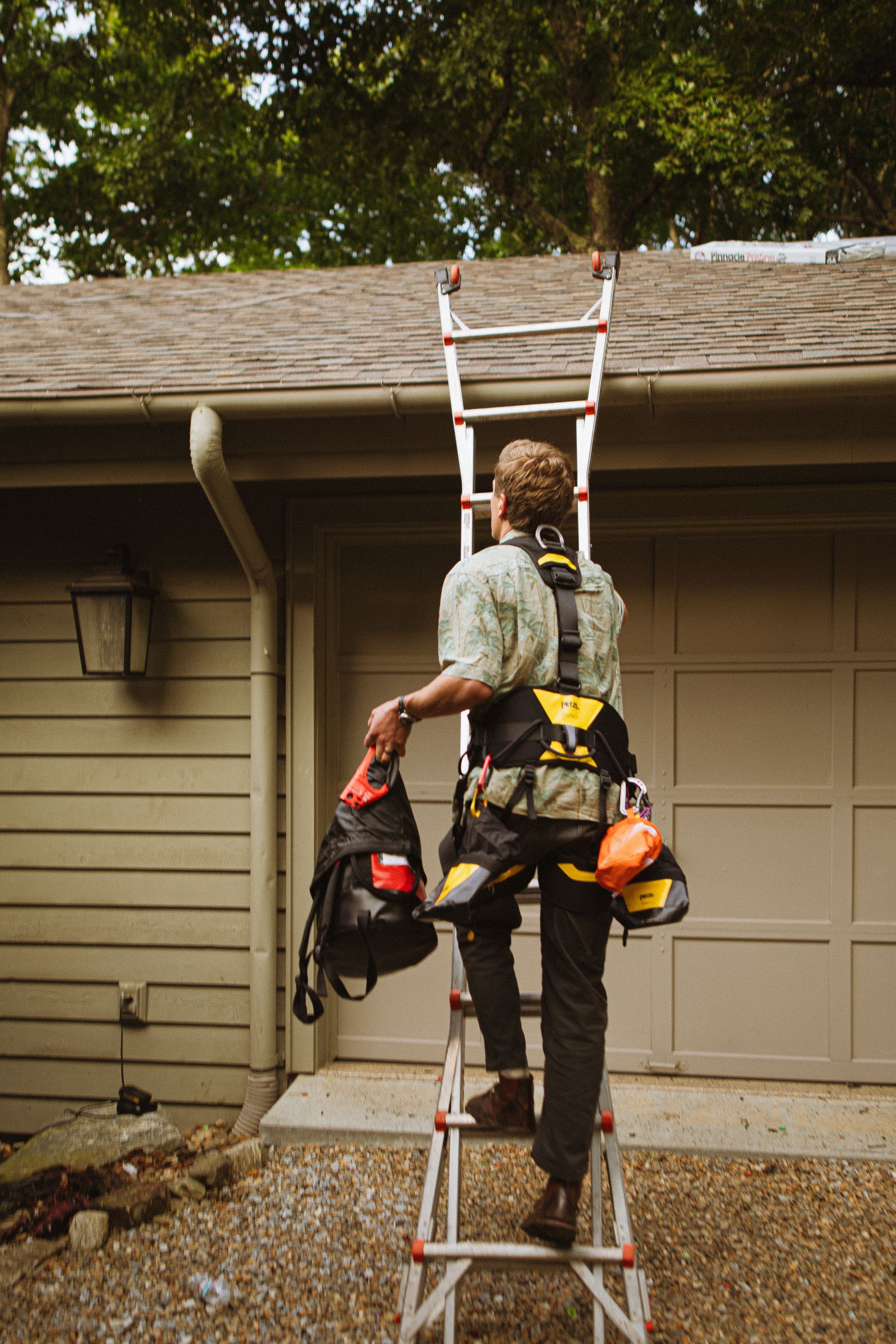 Roofer in a safety harness climbing a ladder to the roof edge