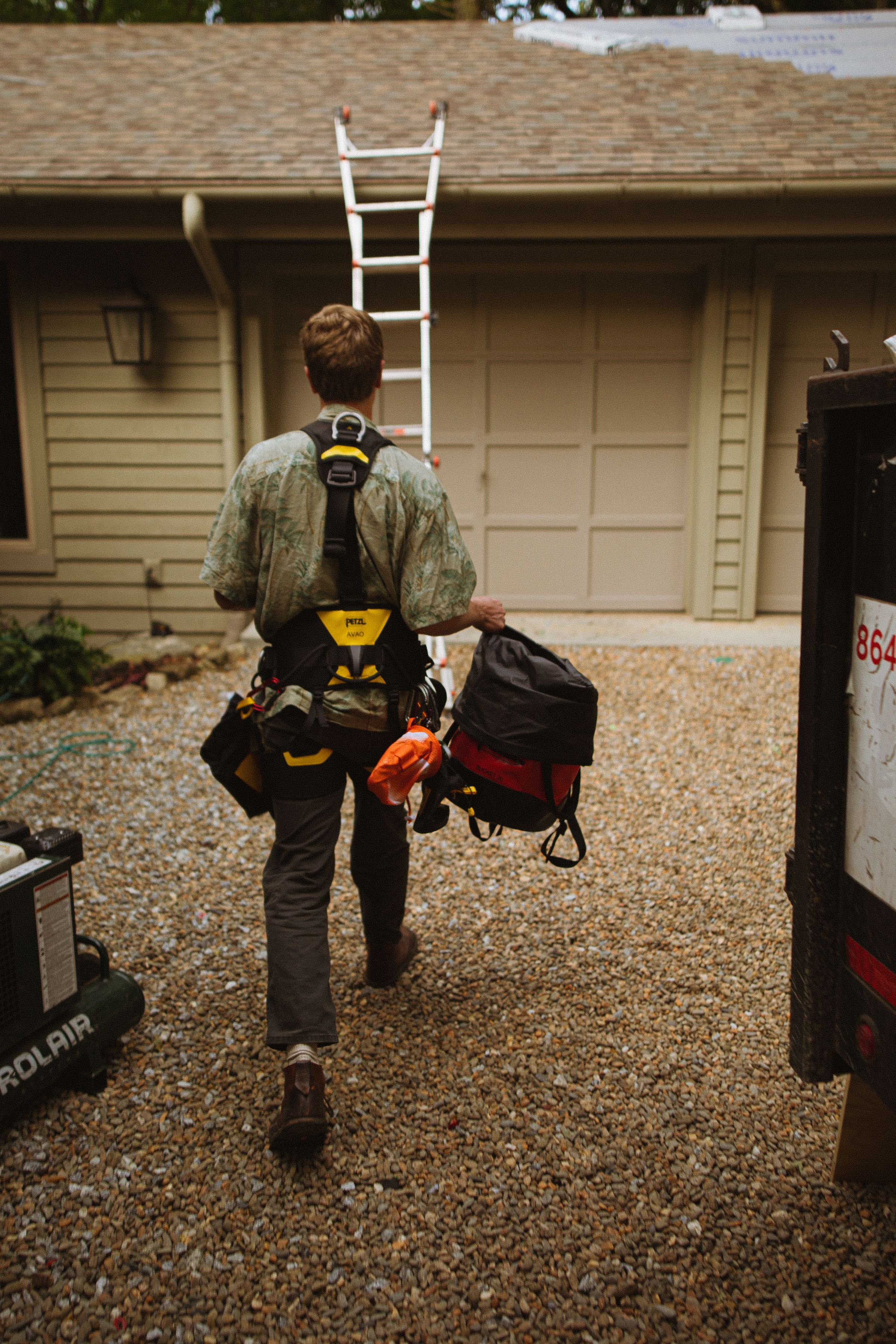 Roofer in a harness walking up the driveway with his gear