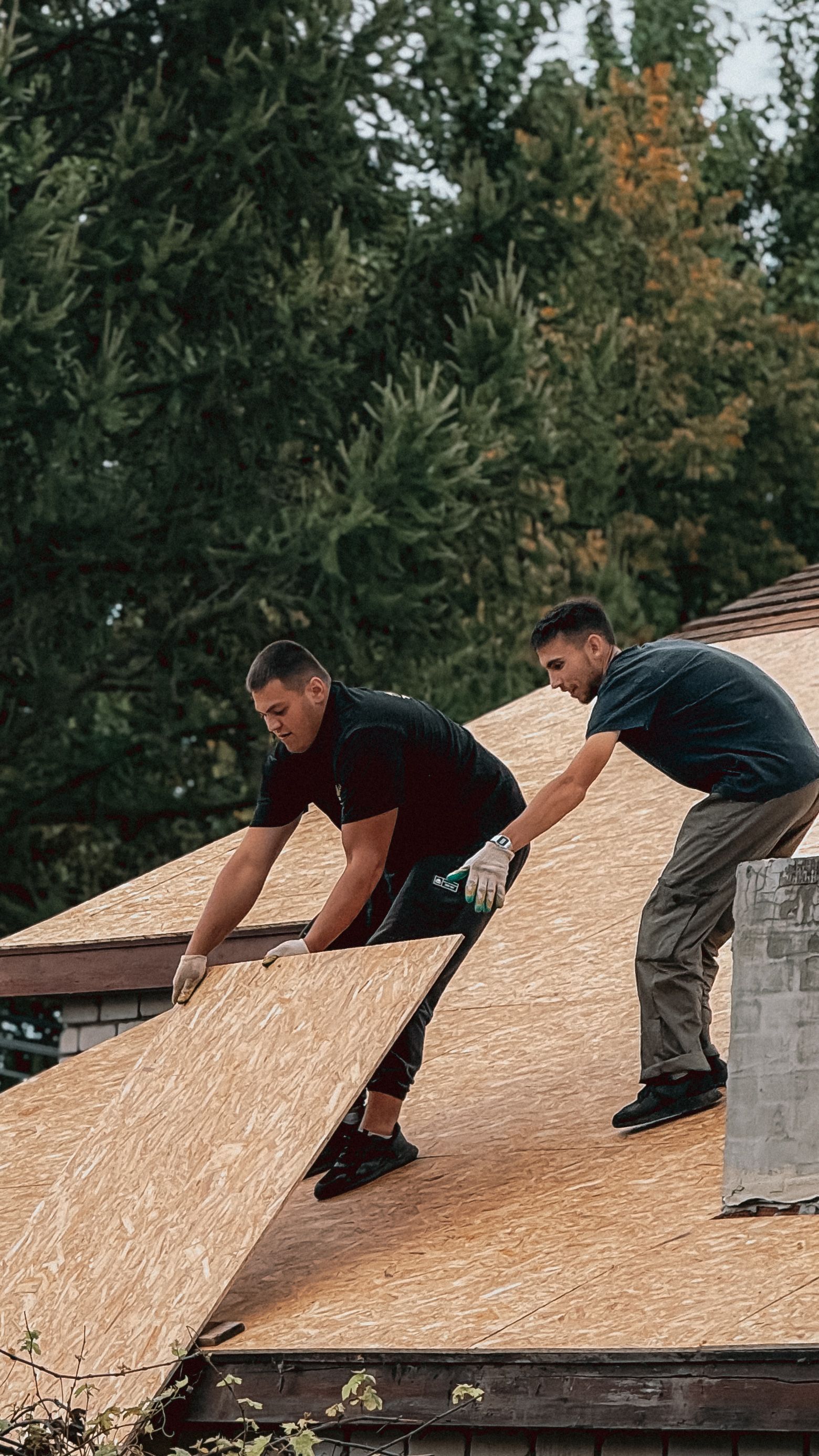 Two roofers fitting a new plywood sheet on the roof deck