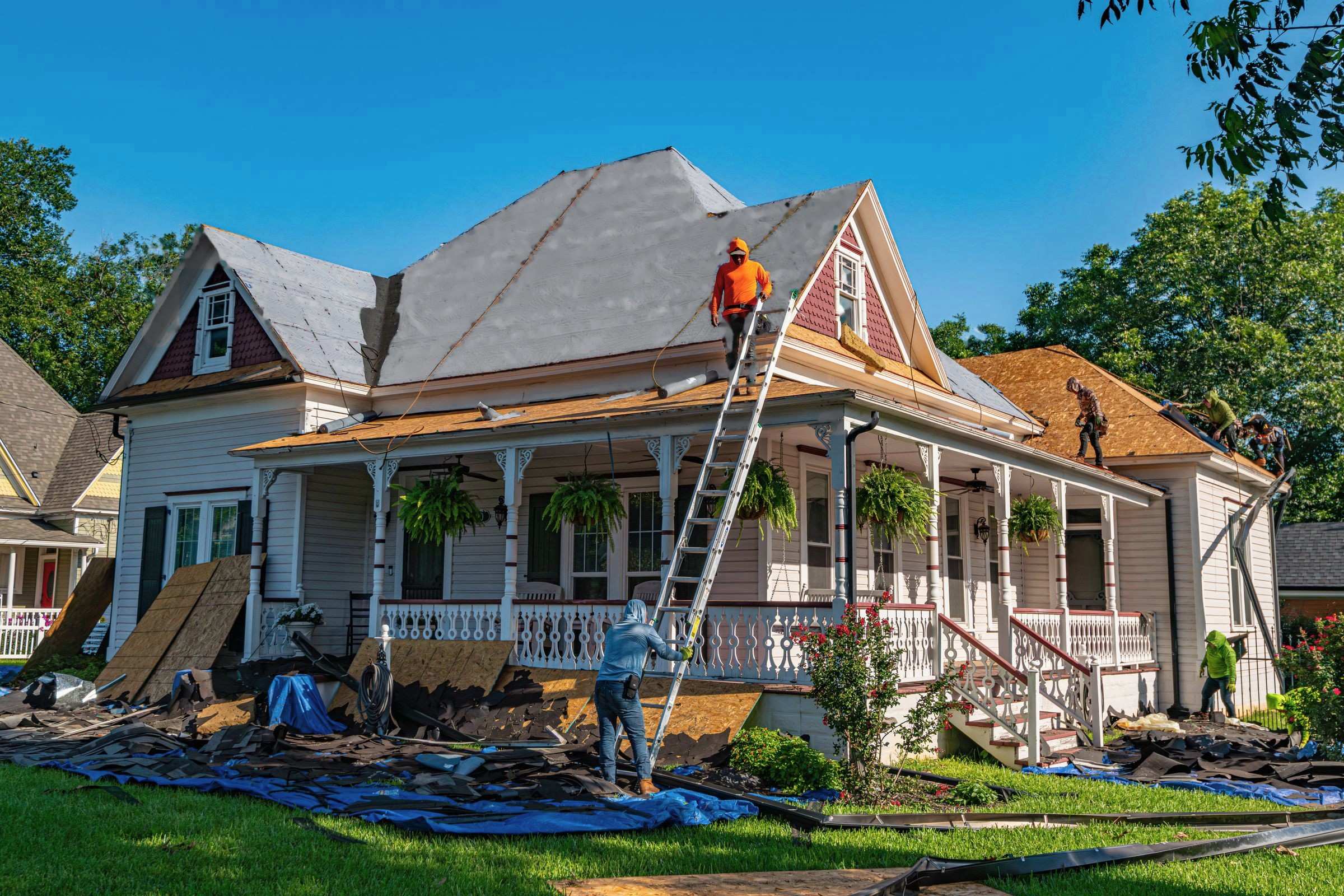 Kestrel crew replacing the roof of a white two-story house with a wraparound porch; tarps cover the lawn